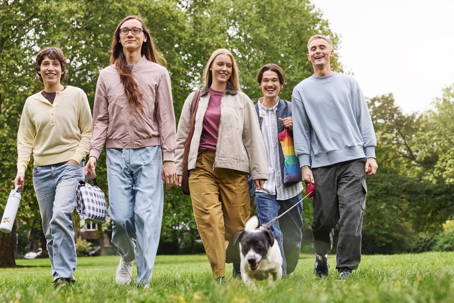 5 Personen-Gruppe, die lächelnd mit einem Hund in einem Park spazieren.
