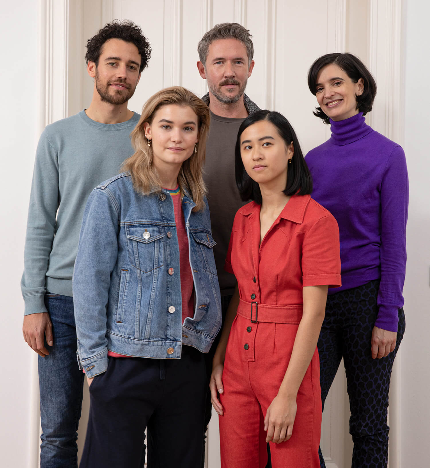 Eine Gruppe unterschiedlicher Personen steht zusammen vor einer Wand und blickt nach vorne.