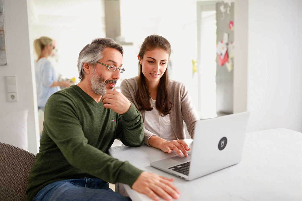 Ein Vater sitzt mit seinem Kind an einem Tisch, auf dem ein Laptop steht.