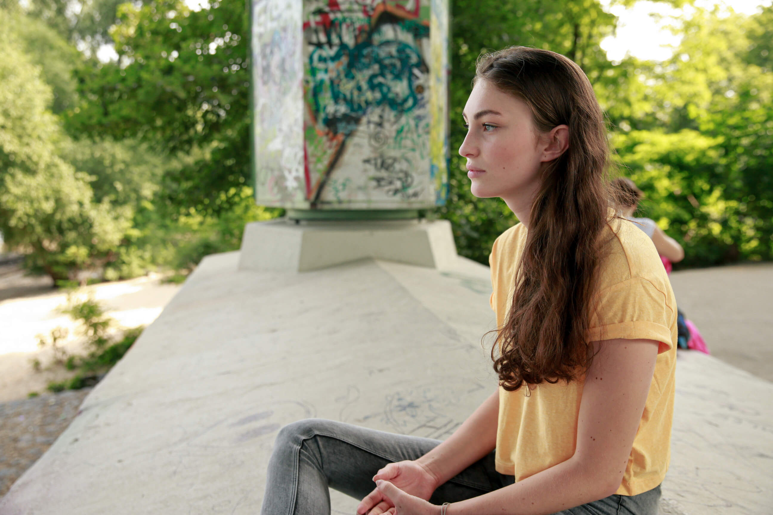 Eine junge Frau sitzt in einem Park und schaut nachdenklich in die Ferne.