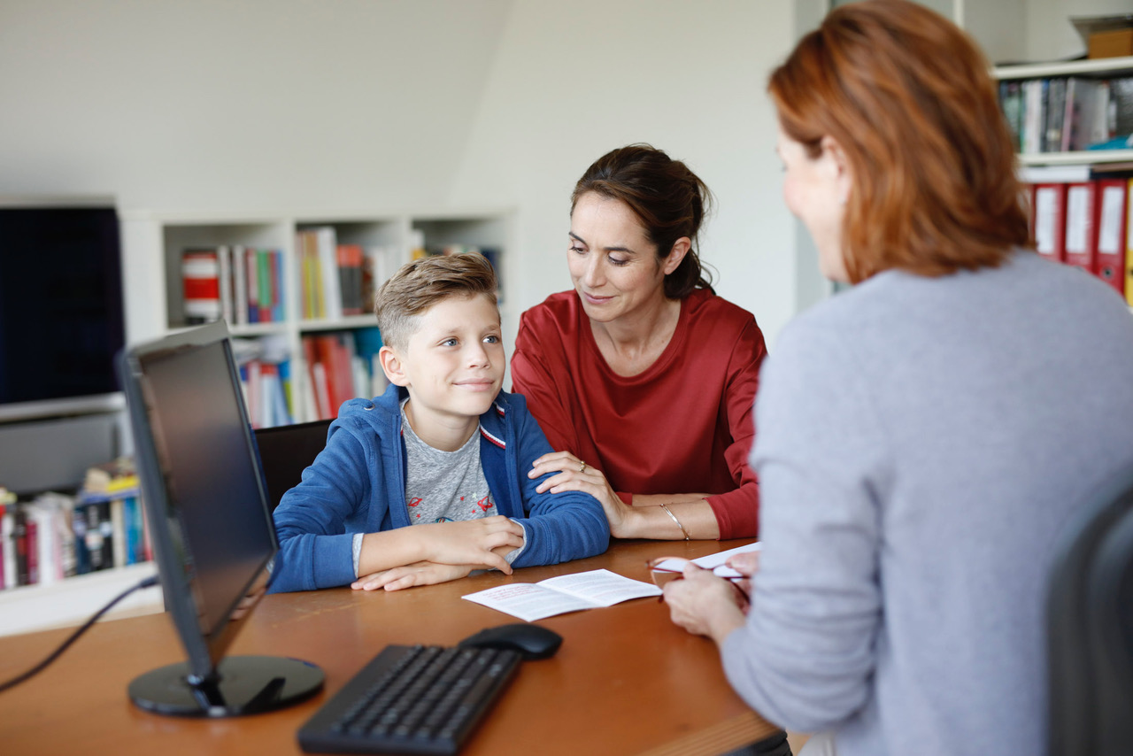 Ein Kind ist mit dessen Mutter bei einer Ärztin und schaut die Ärztin lächelnd an.