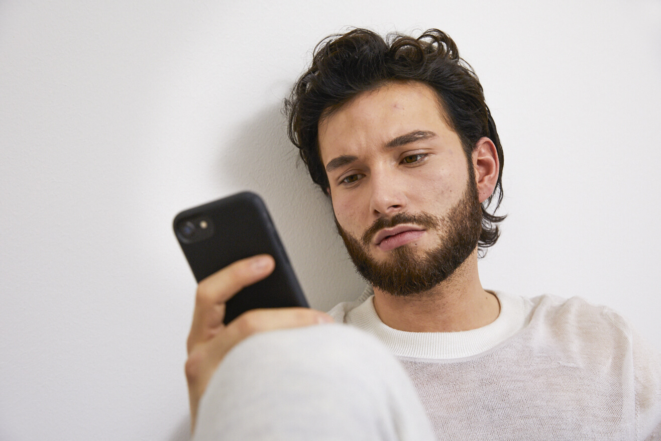 Ein junger Mann schaut nachdenklich auf sein Smartphone.