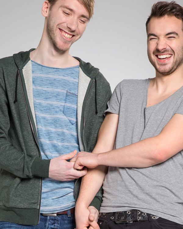 Schwules Paar lacht einander an und hält Händchen.