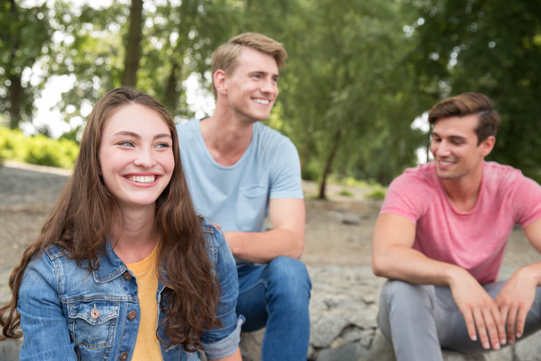 Eine gemische Gruppe junger Menschen sitzt gemeinsam gut gelaunt im Park.