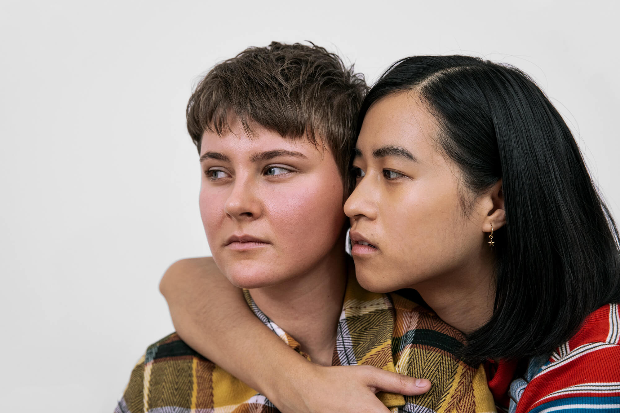 Zwei junge Frauen umarmen sich und blicken nachdenklich zur Seite.