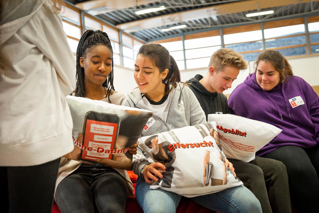 Vier Schülerinnen und Schüler haben Kissen in der Hand, auf denen die Schlagworte »Online-Dating«, »Eifersucht« und »Abgeblitzt« stehen.