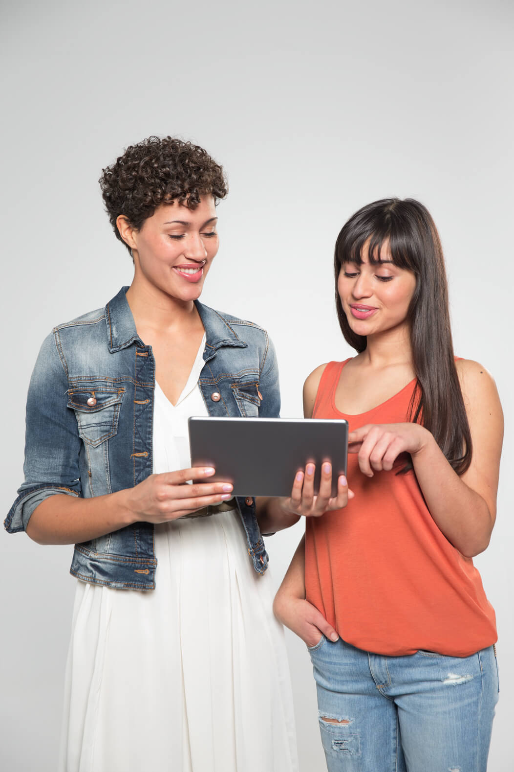 Zwei Freundinnen schauen gemeinsam auf ein Tablet, eine der Frauen erklärt etwas.