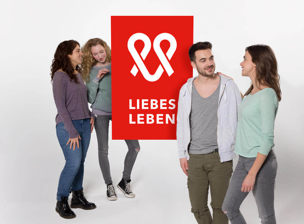 Eine Gruppe steht um das Logo der Kampagne LIEBESLEBEN und unterhält sich.