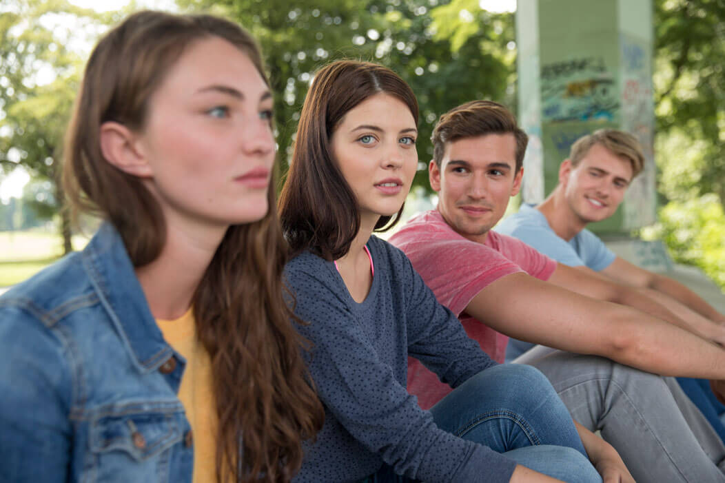 Eine Gruppe junger Menschen sitzt gemeinsam im Park. Zwei der Personen schauen ernst. 