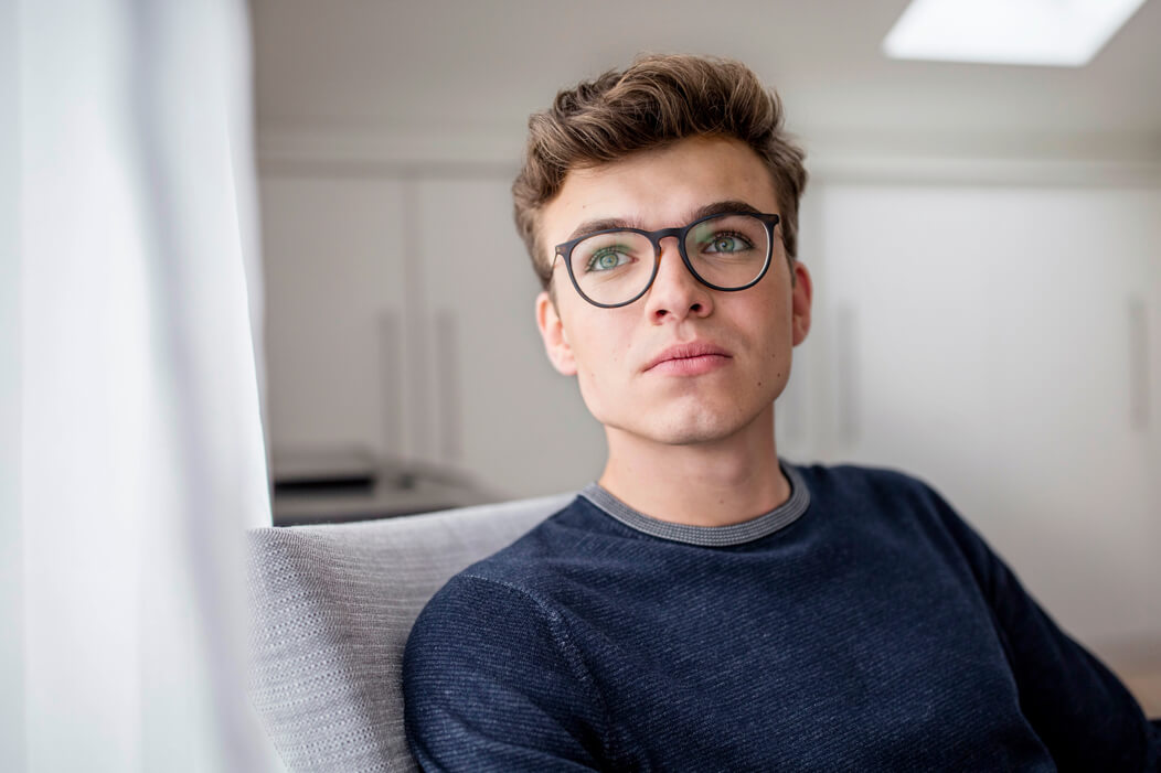 Junger Mann mit Brille schaut nachdenklich in die Luft.