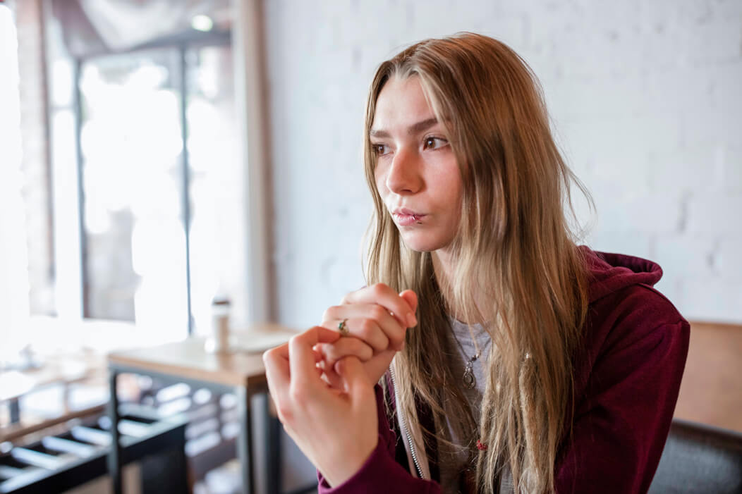 Junge Frau sitzt in einem Cafe und schaut nachdenklich.