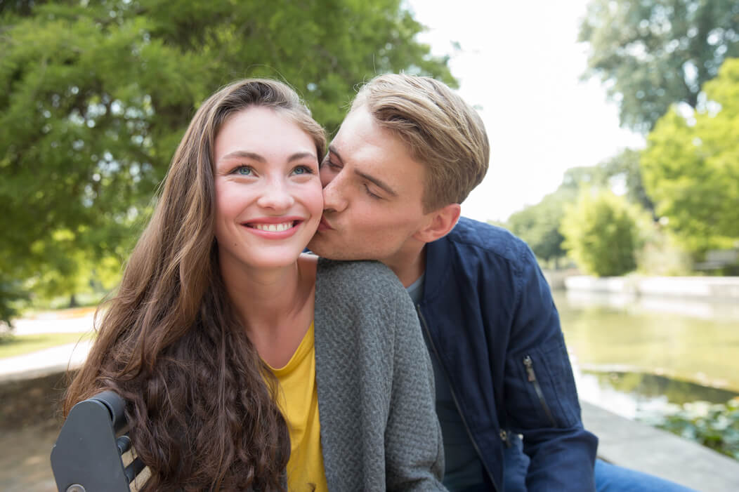 Junges, heterosexuelles Paar. Der Mann küsst seine Partnerin auf die Wange. Die Frau lächelt.