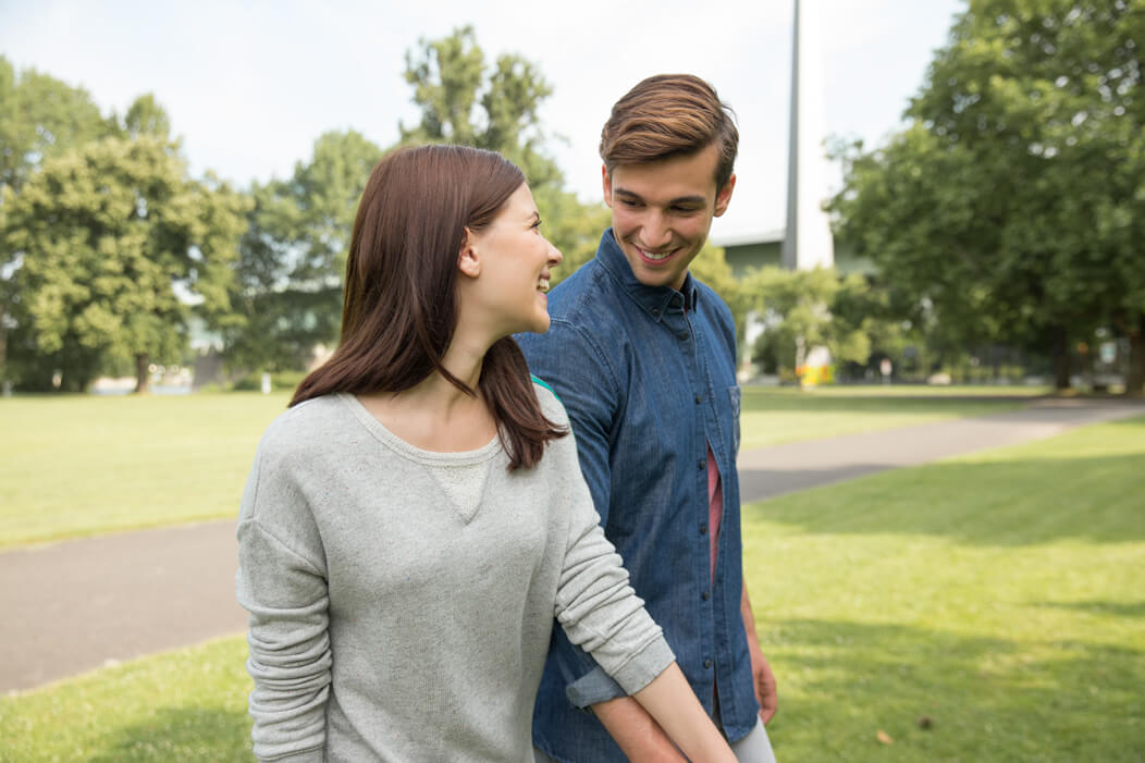 Junges, heterosexuelles Paar lächelt sich an und hält Händchen.