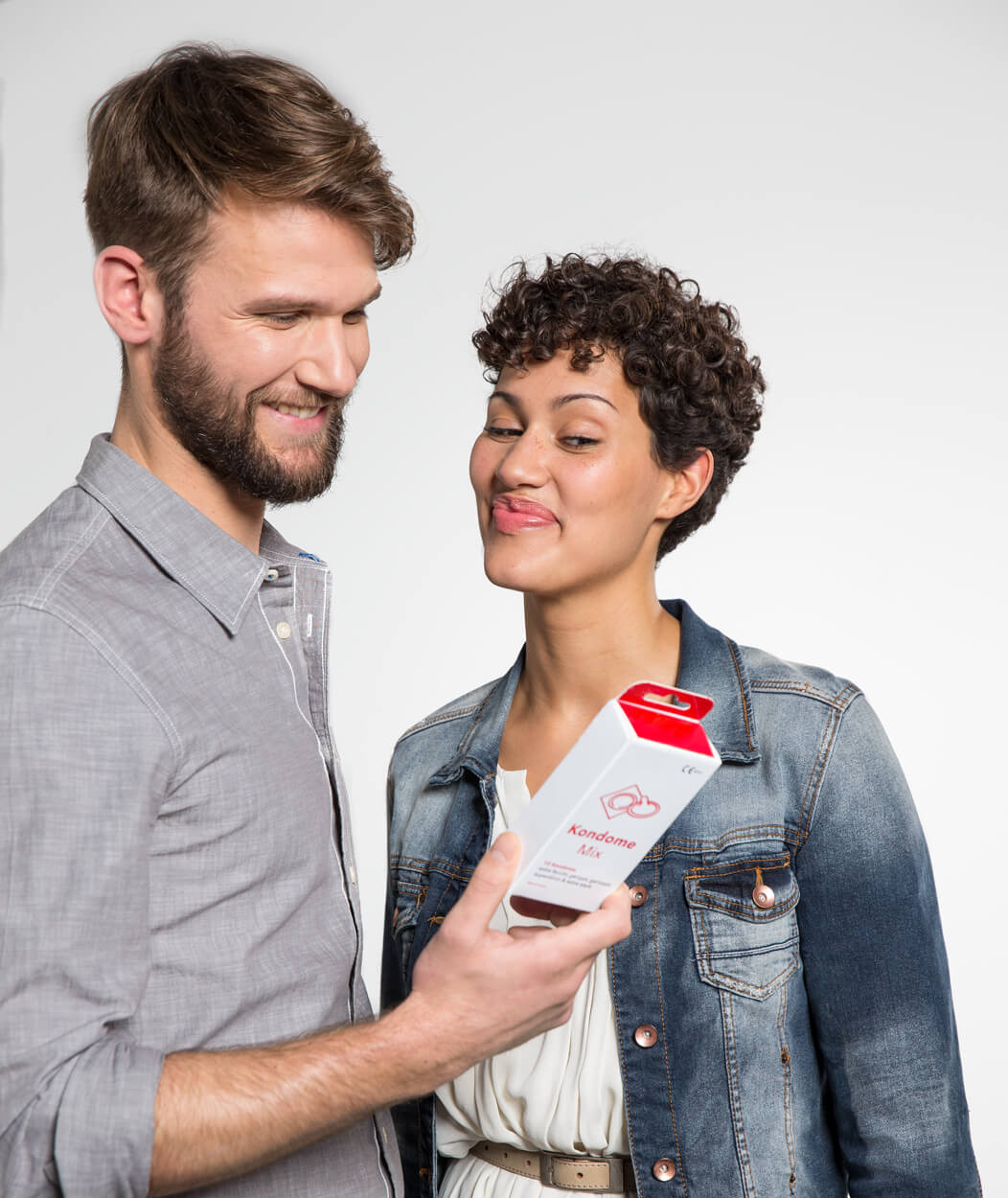 Heterosexuelles Paar schaut lächelnd und zwinkernd auf eine Packung Kondome.