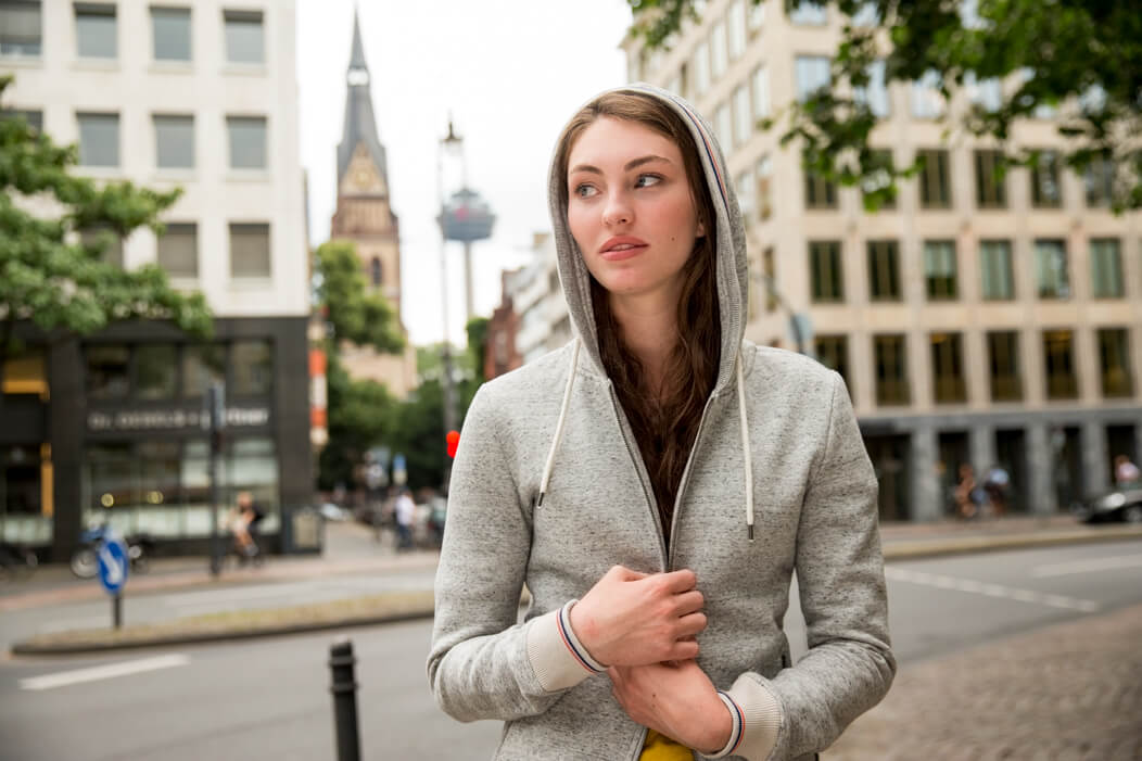 Junge Frau halt schützend ihren Kapuzenpullover zu und blickt aufgewühlt zur Seite.