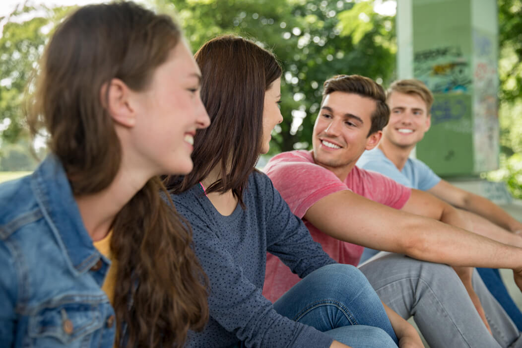 Eine gemische Gruppe junger Menschen sitzt gemeinsam gut gelaunt im Park.