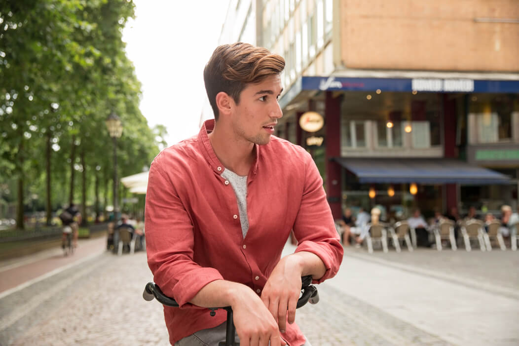 Junger Mann sitzt auf Fahrrad und schaut sich mit entspanntem Gesichtsausdruck um.