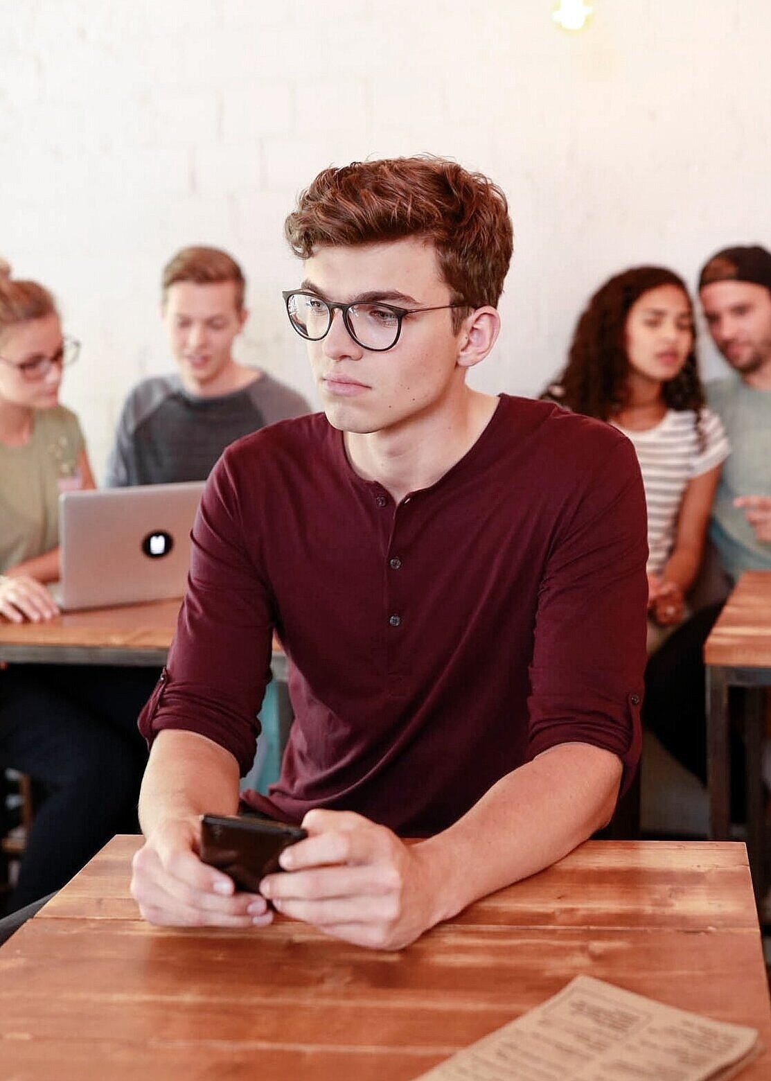 Ein junger Mann sitzt in einem Café und schaut nachdenklich auf sein Handy.