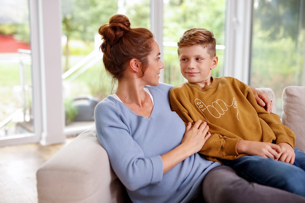 Das Bild zeigt eine Mutter mit ihrem Kind, die zusammen auf dem Sofa sitzen und sich unterhalten.